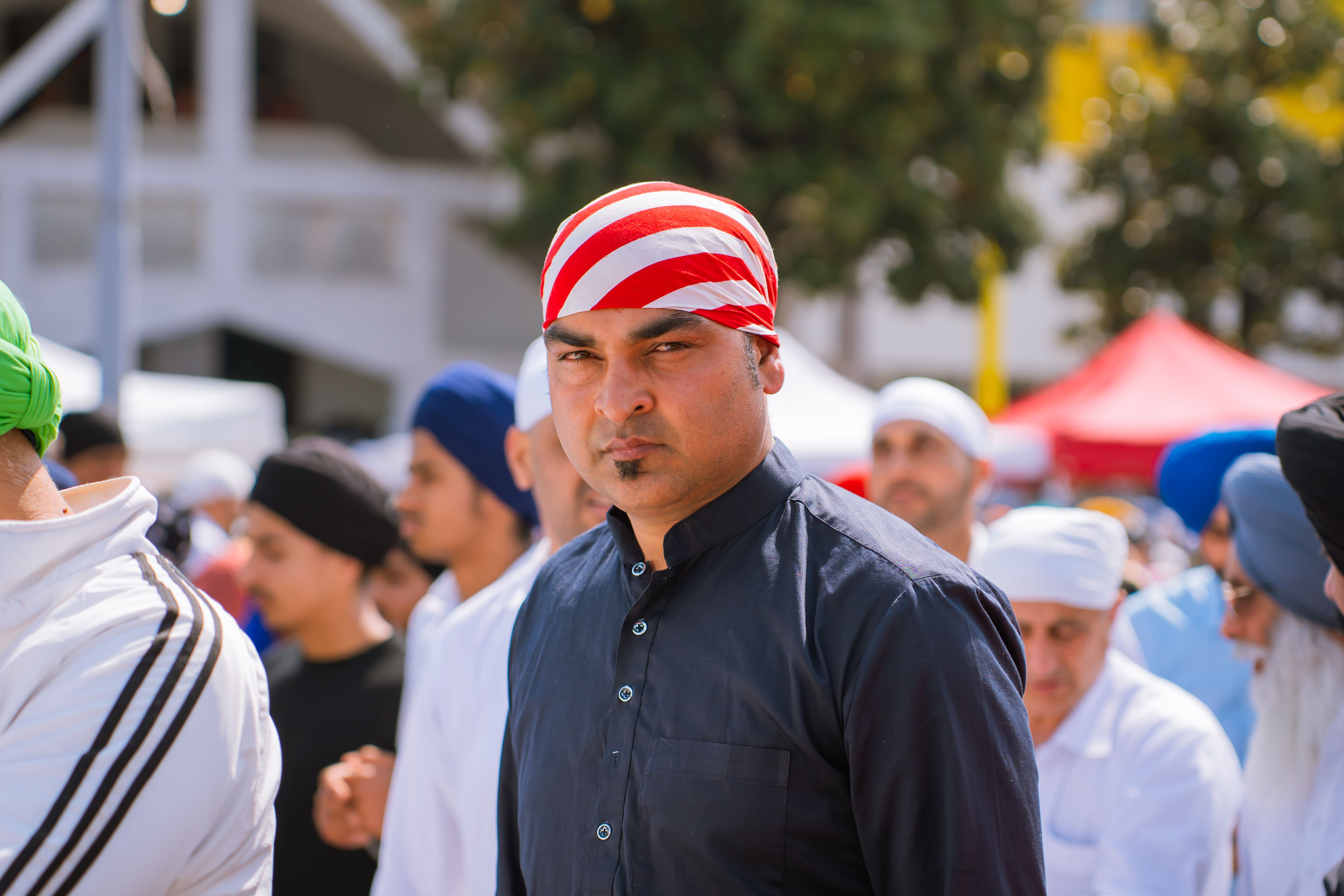 A man wearing a red and white striped turban in a crowd at an outdoor cultural event.