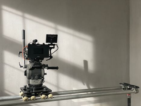 A high-end professional camera mounted on a dolly track in a studio with soft lighting and shadows.