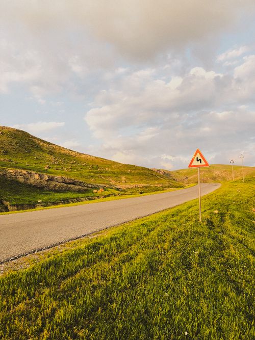 Free Scenic mountain road featuring a sharp turn warning sign under a cloudy sky, ideal for travel themes. Stock Photo