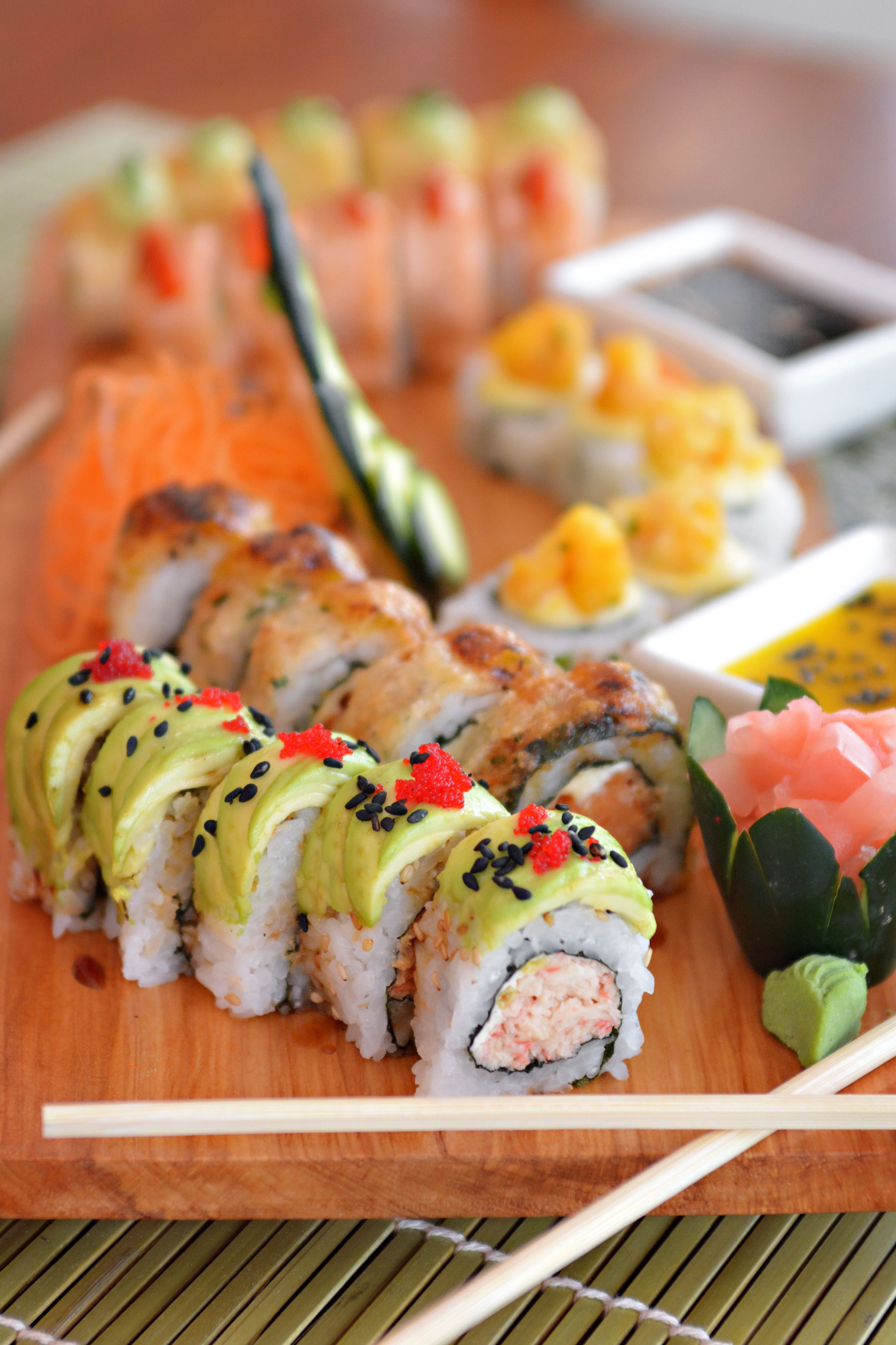 Six pieces of nigiri including salmon, tuna, and shrimp, each a hand-pressed oval of vinegared rice topped with a single slice of fish, arranged on a dark wooden board with a small dish of soy sauce.