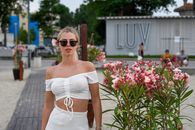 Stylish woman in white summer outfit posing at LUV Beach with pink flowers in Constanța, Romania.