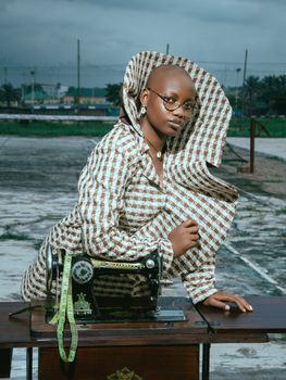 A stylish designer poses with a vintage sewing machine outdoors, showcasing creativity and style.