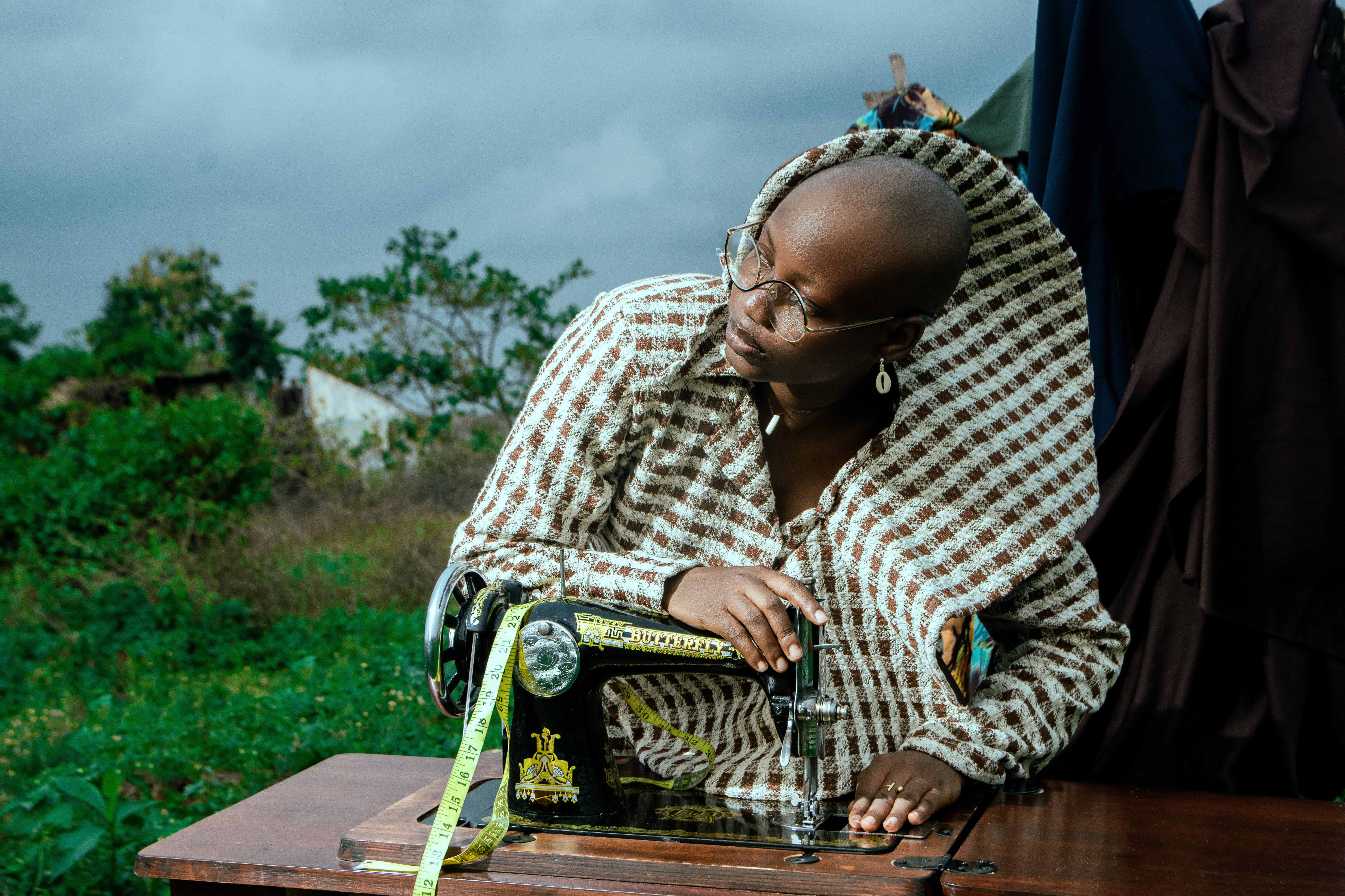A tailor focuses on work using a vintage sewing machine in an outdoor setting.
