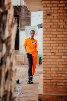 A young person in colorful clothing standing confidently outdoors by a brick wall.