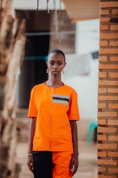 Portrait of a stylish woman in a bright orange zip-up outfit standing near a brick wall outdoors.