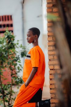 A young woman in vibrant orange clothing stands outdoors against a brick wall.
