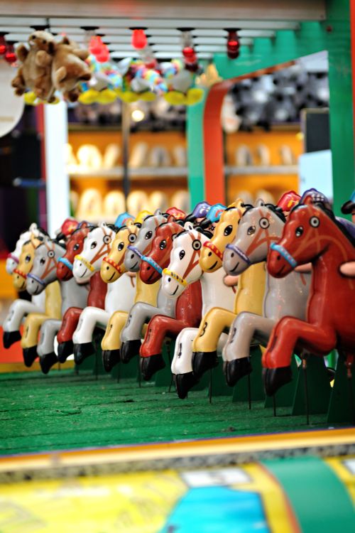Free A vibrant line of carousel horses in an amusement park setting, evoking fun and nostalgia. Stock Photo
