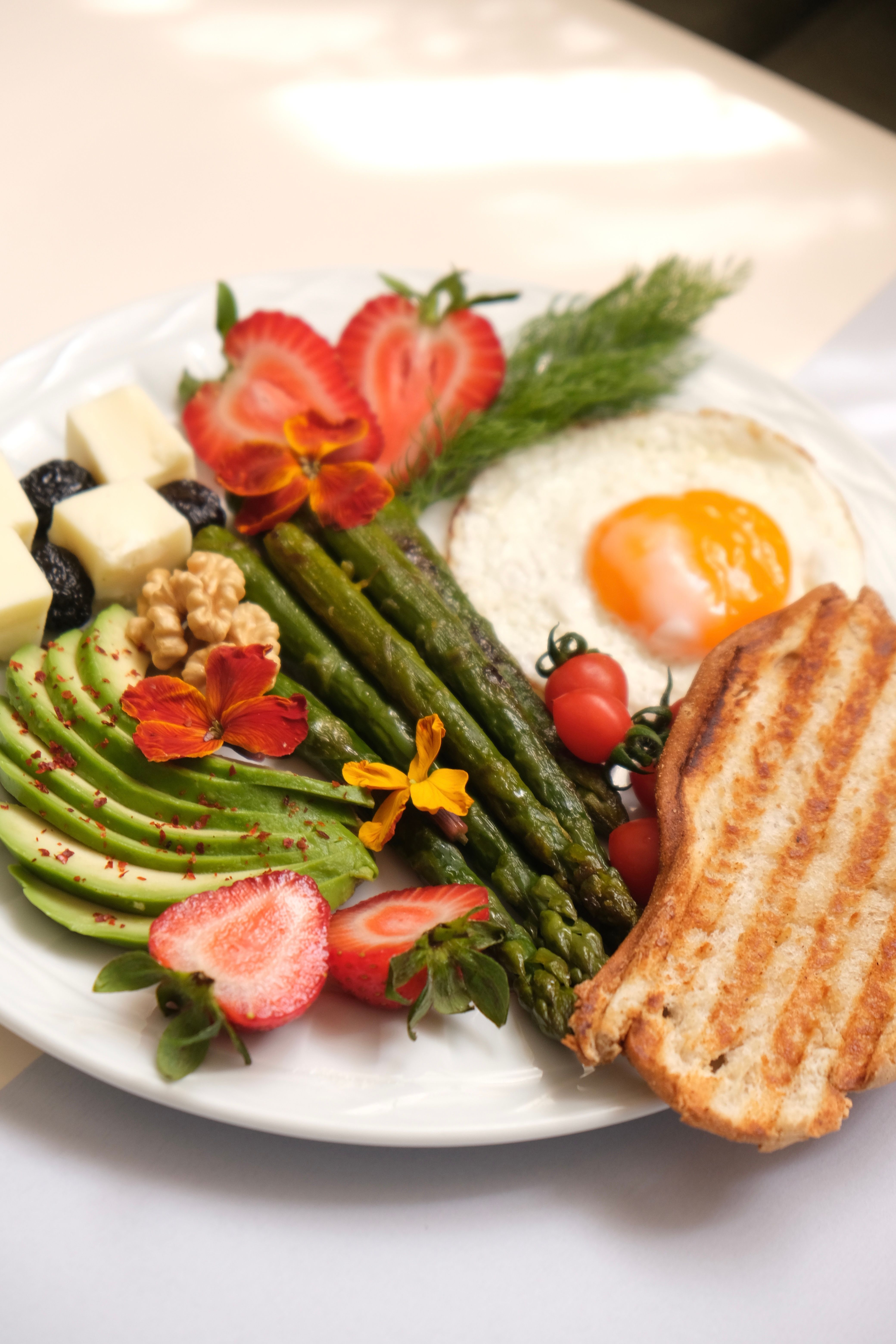A nutritious breakfast plate with avocado, egg, strawberries, and toast.
