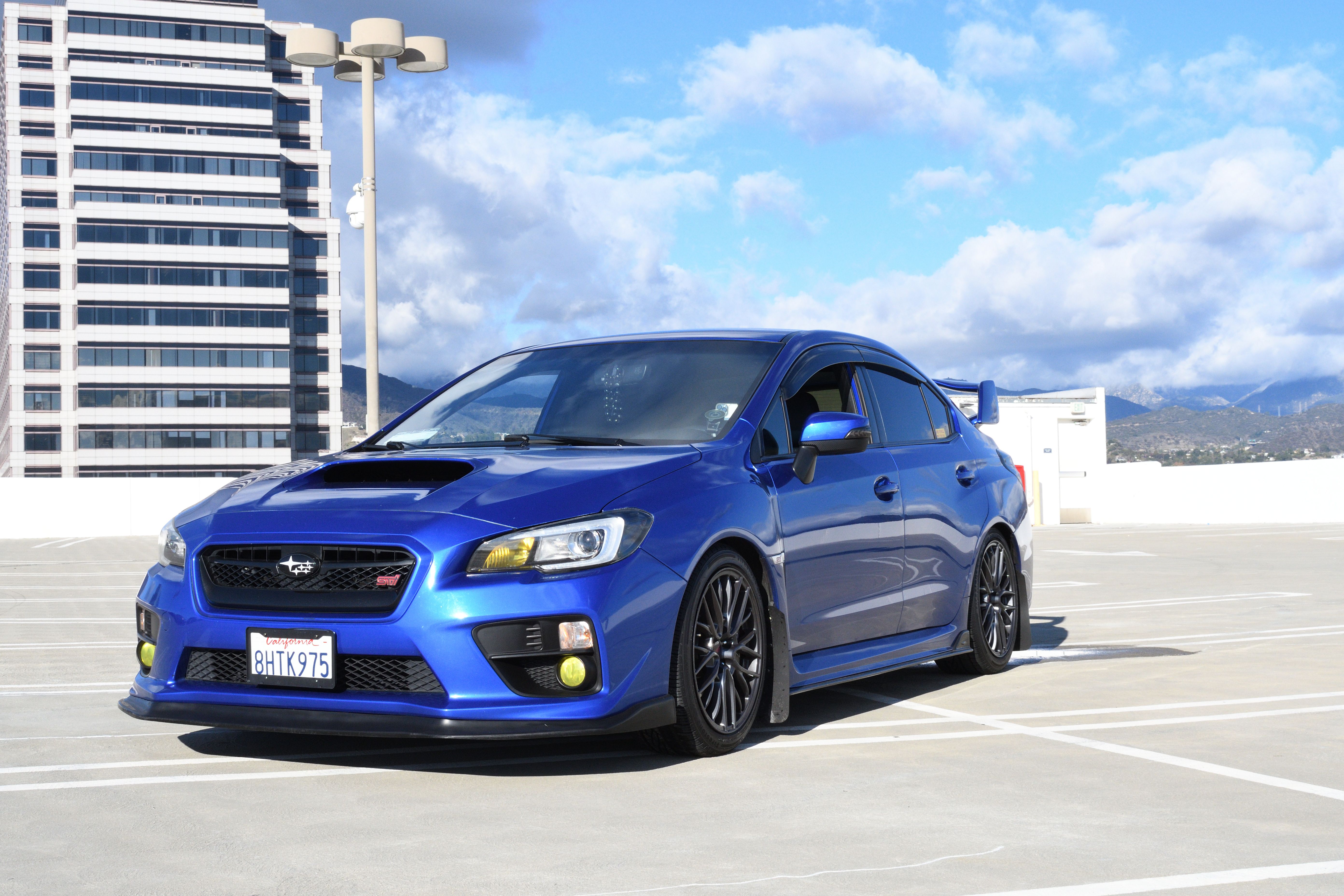 A striking blue sports car parked on a rooftop with city skyline.