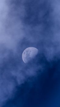 Half moon partially obscured by dramatic clouds, creating a mysterious night sky scene.