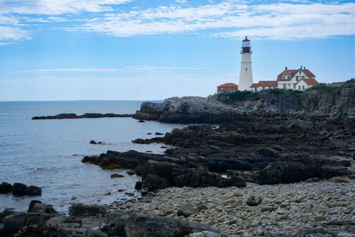 Free Scenic view of the iconic Portland Head Light on a rocky coast in Cape Elizabeth, Maine, under a bright blue sky. Stock Photo
