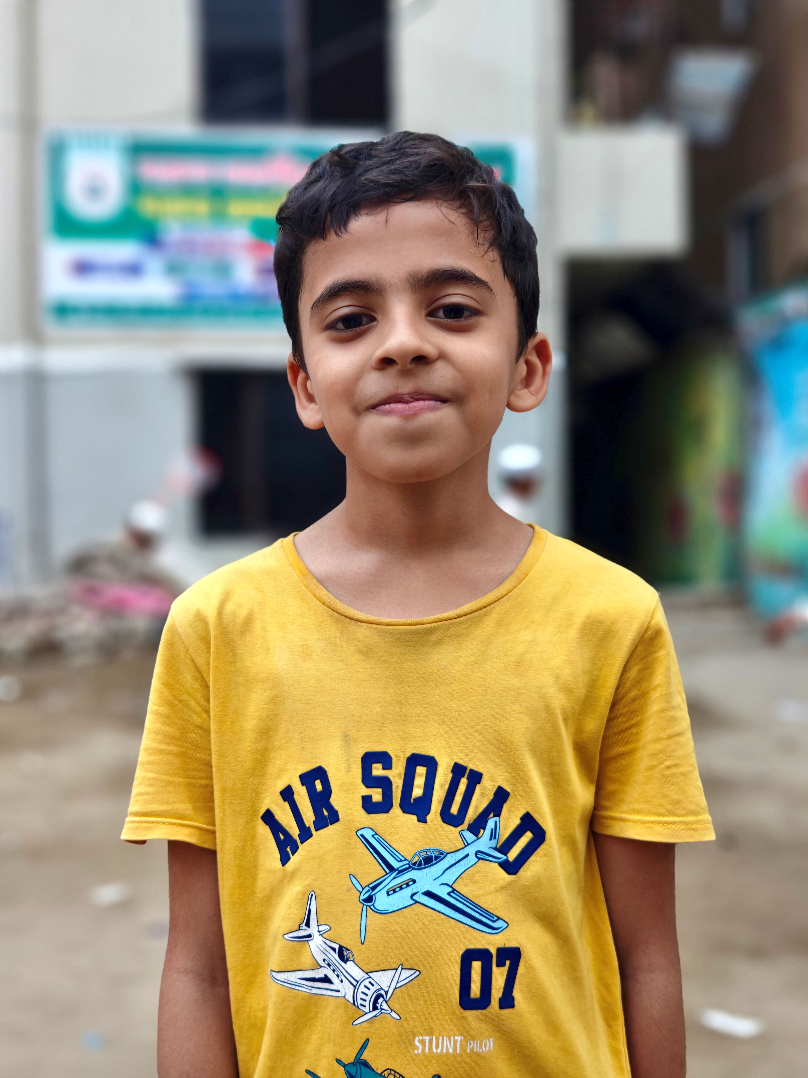Young boy in yellow airplane t-shirt smiling confidently outdoors.