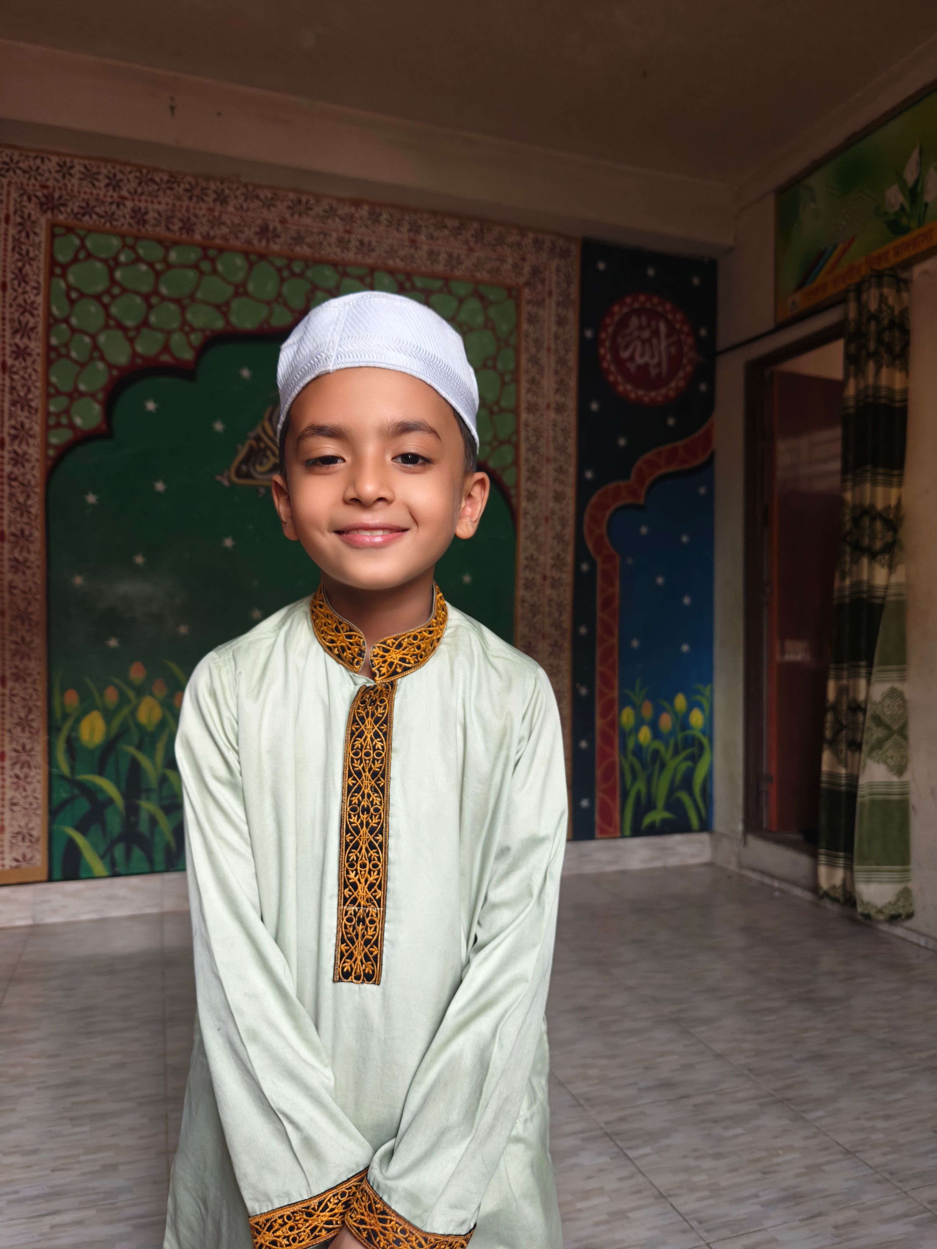 Smiling boy wearing traditional clothing with a serene backdrop indoors.