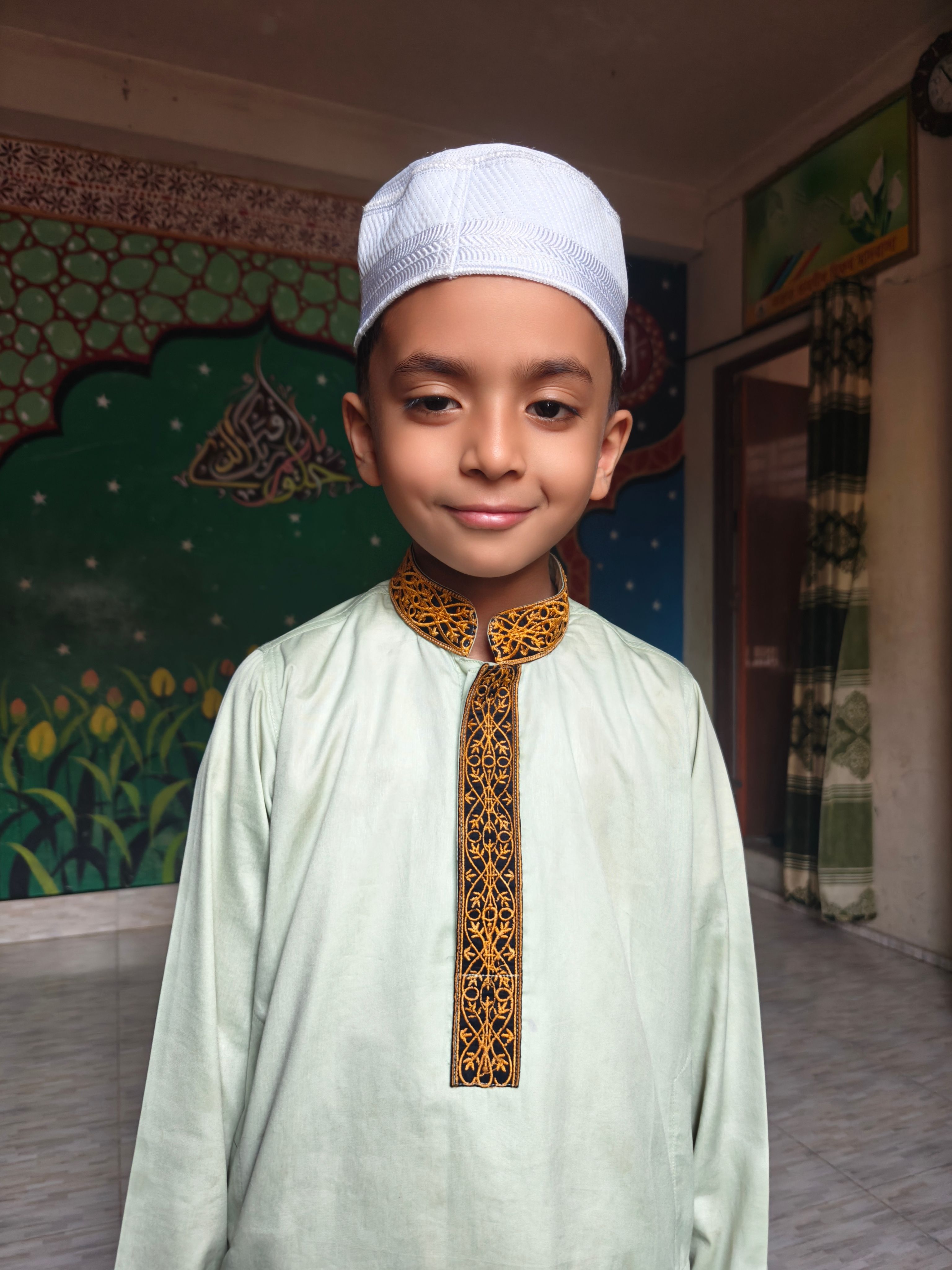 Portrait of a young boy wearing traditional Islamic clothing, indoors with a colorful background.