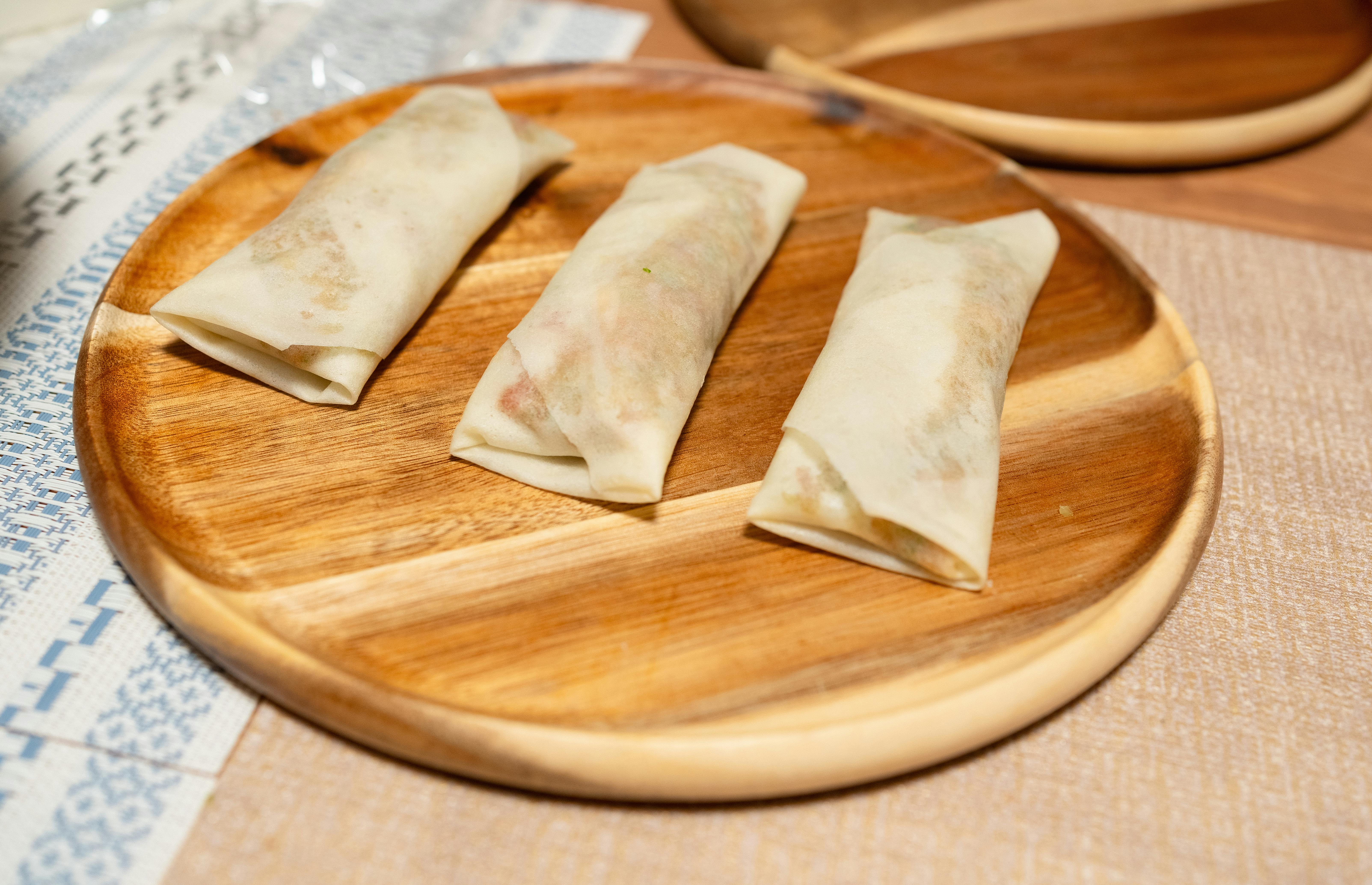 Three freshly made spring rolls placed elegantly on a wooden plate, perfect for Asian cuisine lovers.
