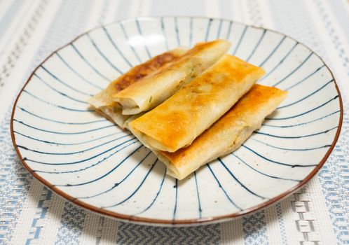 Delicious crispy Asian spring rolls served on a decorative blue-striped plate.
