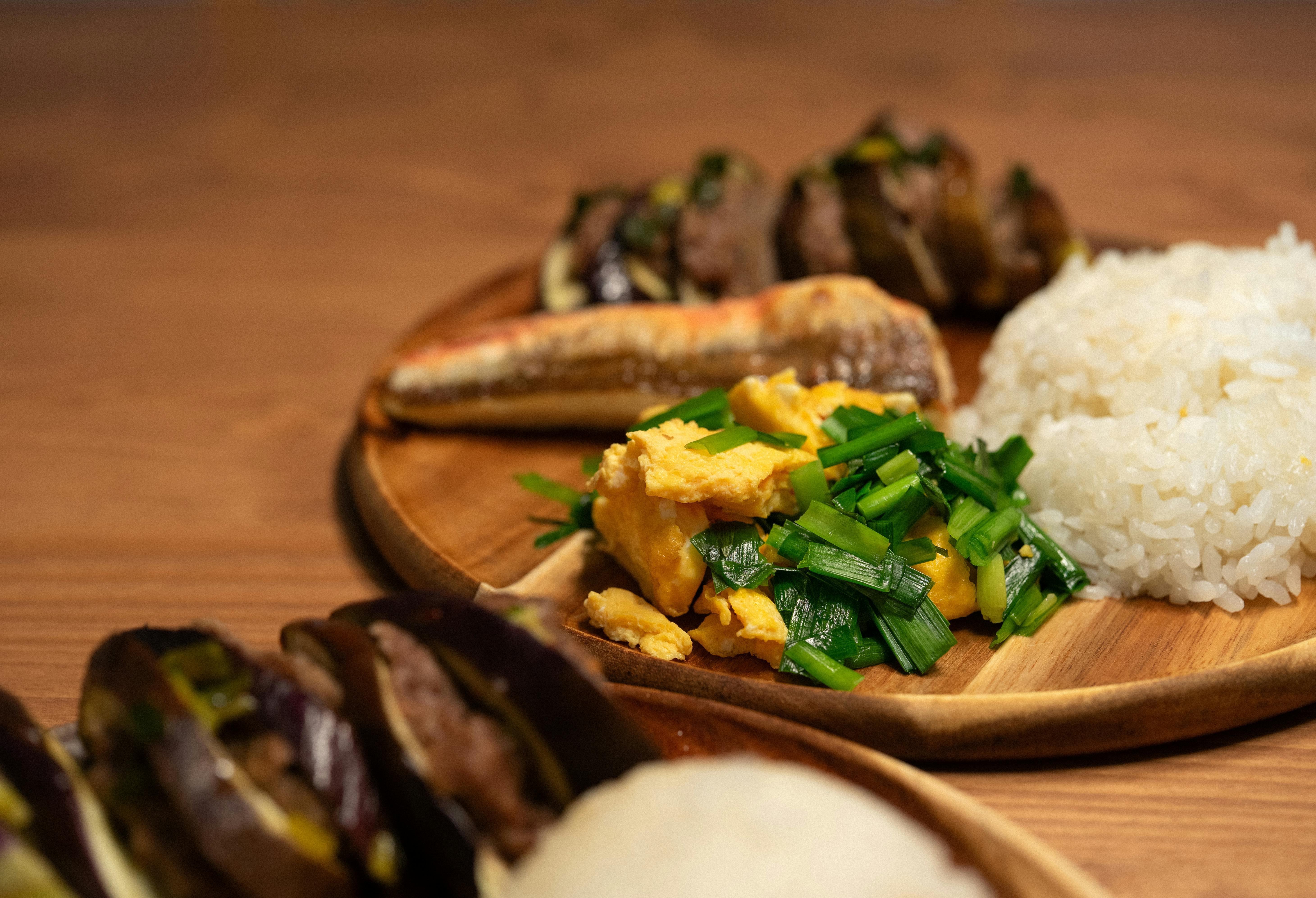 Delicious Asian meal featuring rice, vegetables, and grilled fish on a wooden plate.