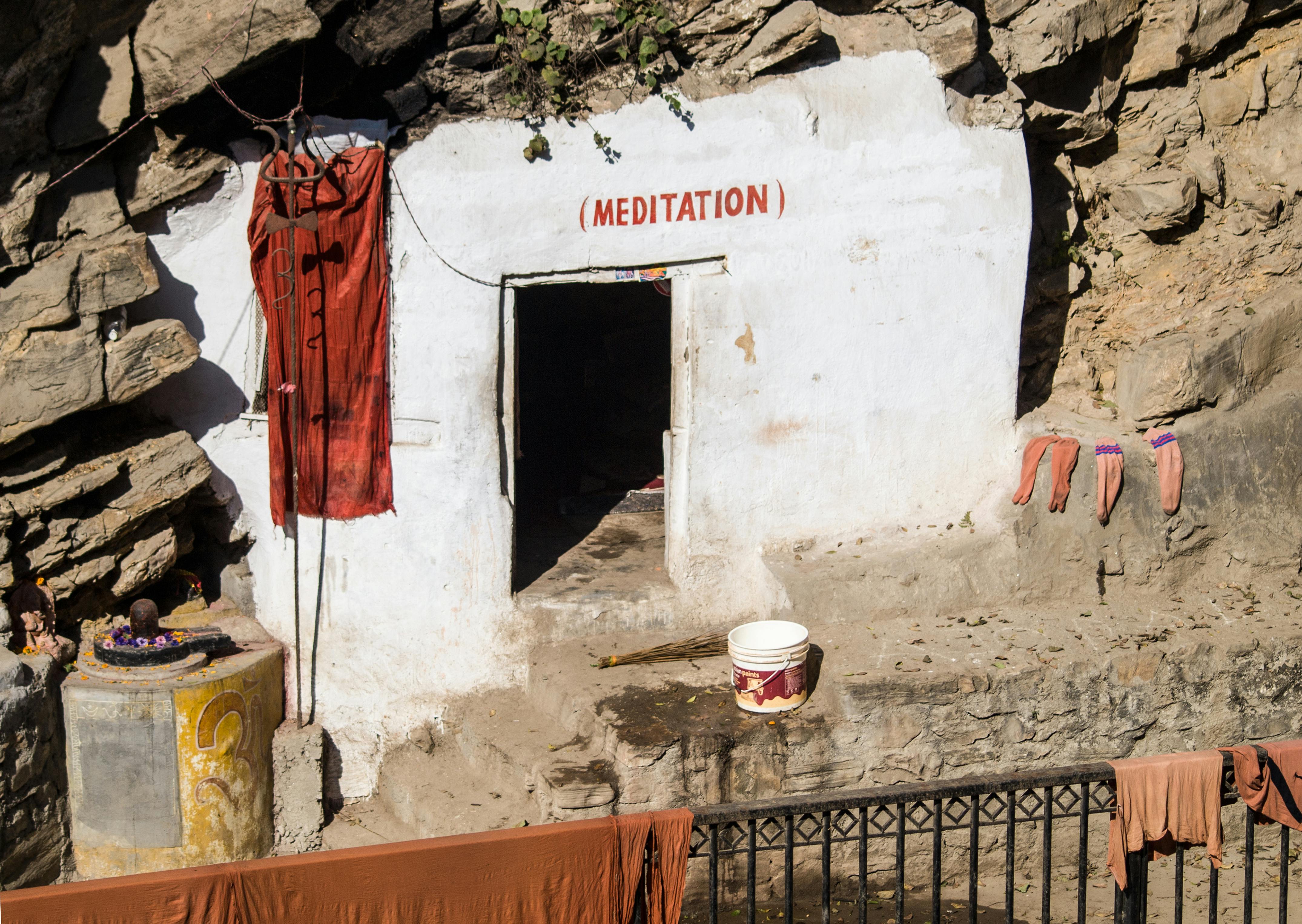 A meditation cave entrance in a rocky landscape adorned with spiritual items.