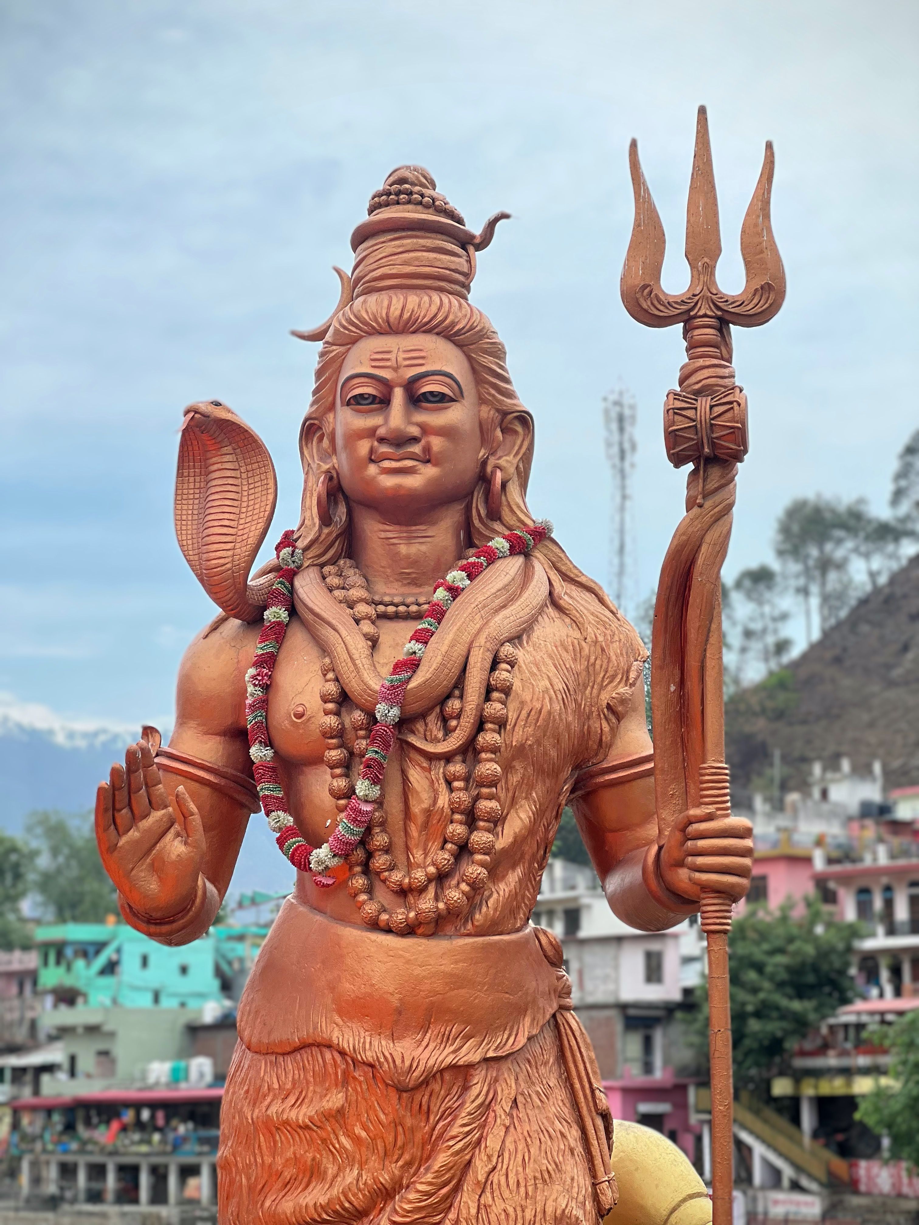 A grand statue of Lord Shiva with Trident in Bageshwar, India against a backdrop of colorful buildings.