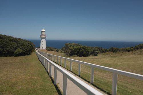 Free A stunning white lighthouse set against a clear blue sky and ocean view with open grassy surroundings. Stock Photo