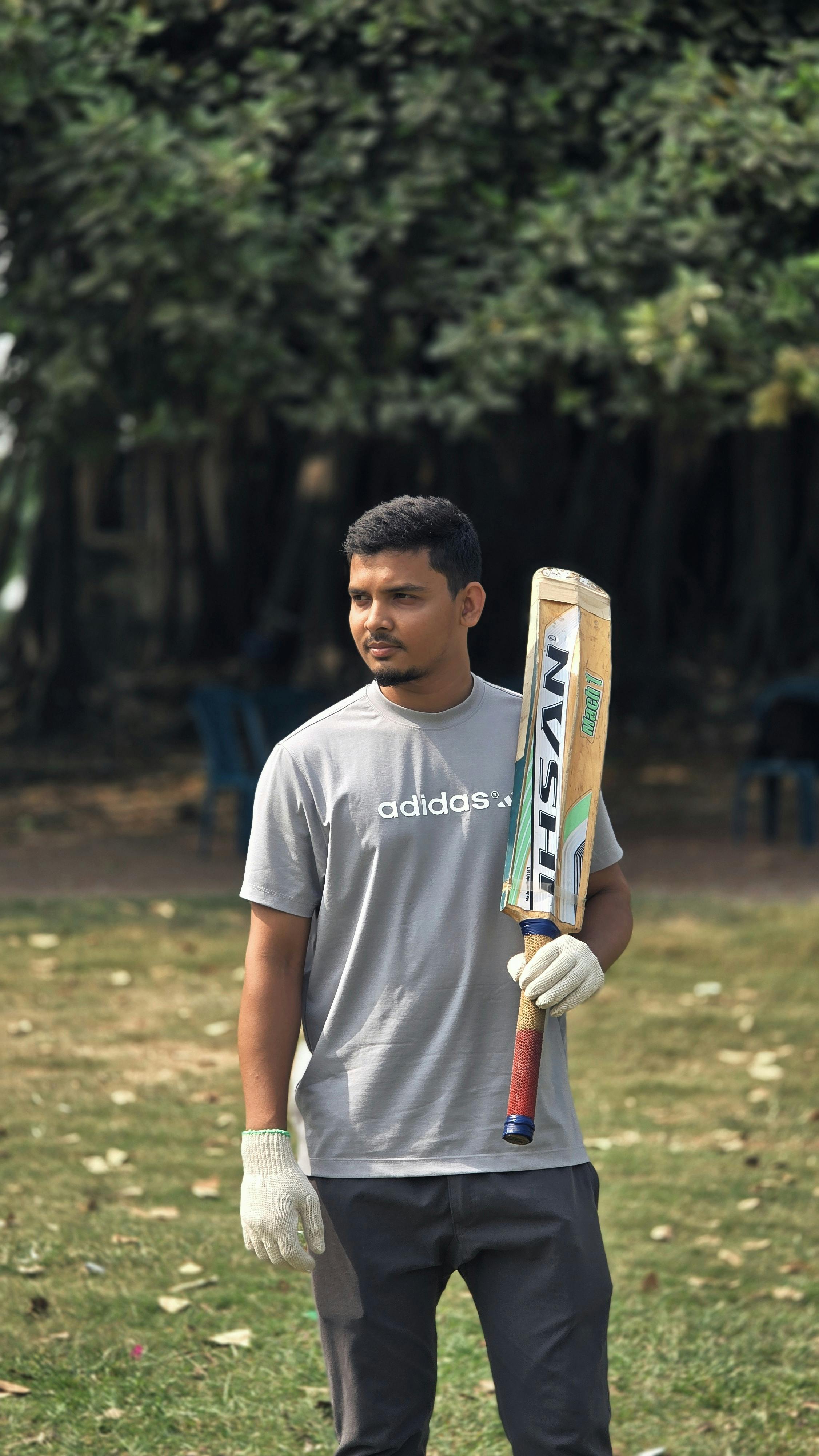 Young man holding a cricket bat in a park, ready to play a game outdoors.