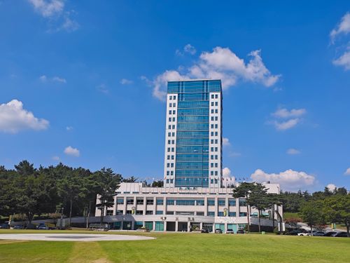 Free Tall office building under clear blue sky, surrounded by trees and grass lawn. Stock Photo