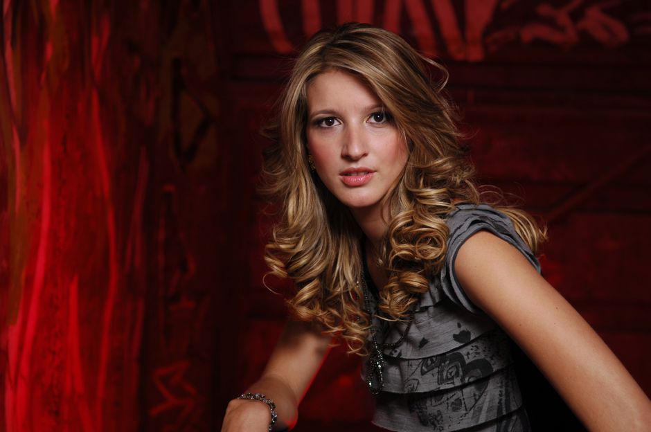 Chic portrait of a young woman with curly hair and a stylish outfit against a red artistic background.
