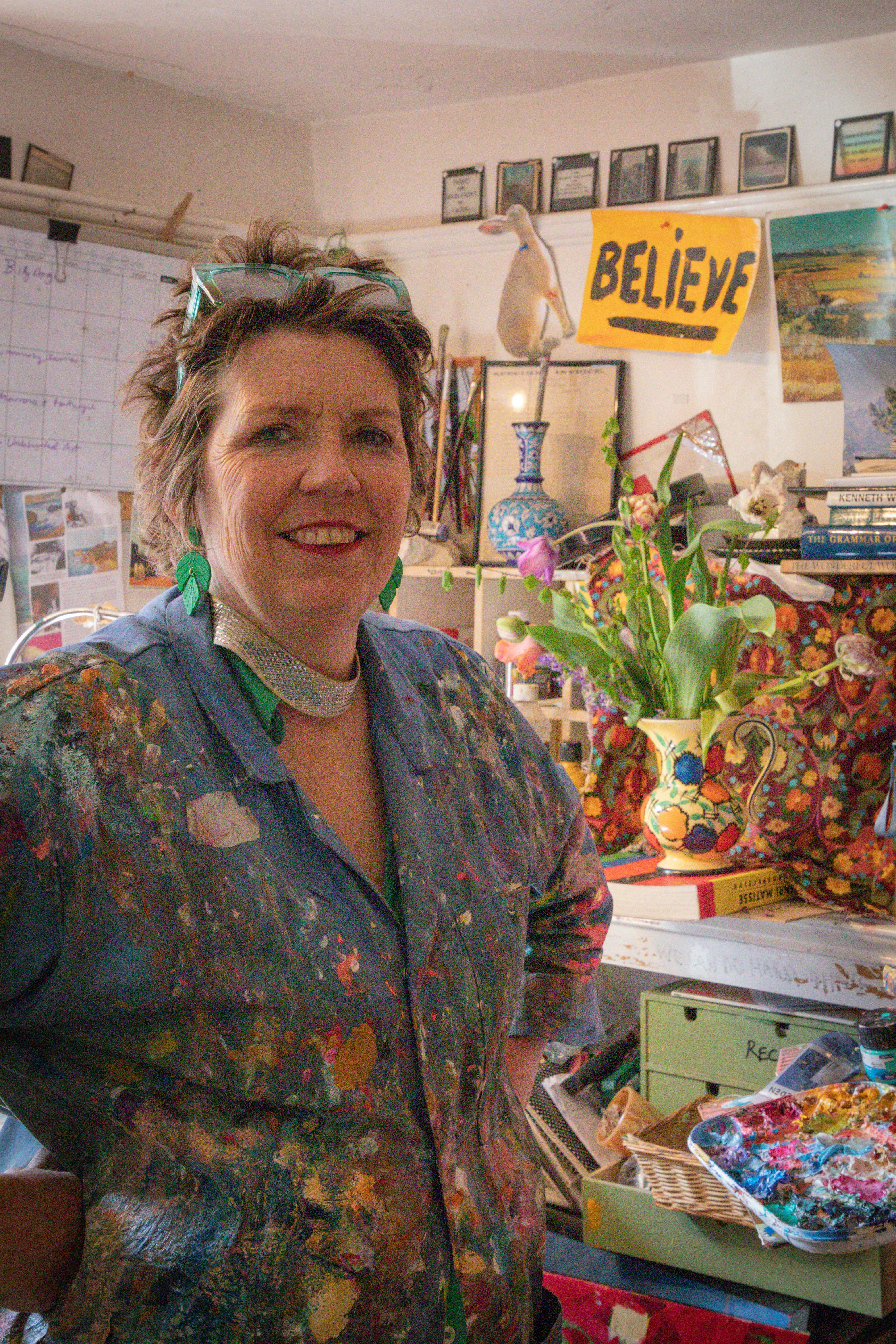 A creative artist stands in a colorful studio surrounded by art supplies and inspirational decor.