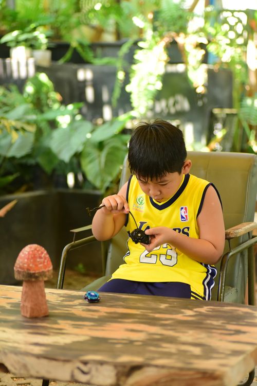 Free Child in jersey plays with toy cars at a garden table, surrounded by plants. Stock Photo