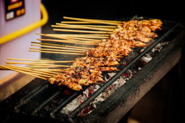 Bamboo skewers of marinated chicken grilling over glowing charcoal on a narrow grill