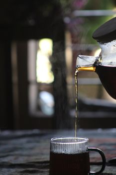 A steaming hot beverage is being poured into a clear glass mug, creating a cozy atmosphere.