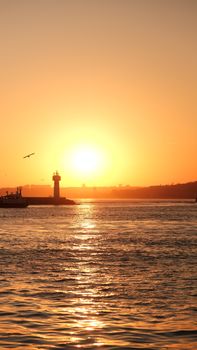 A tranquil sunrise scene with a lighthouse silhouetted against a vibrant ocean horizon.