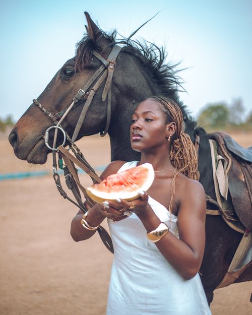 Free Portrait of a woman in Zaria holding watermelon near a horse outdoors. Stock Photo