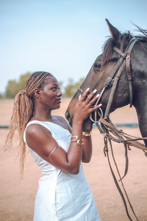 Free Woman in white dress gently touching a horse on a sunny day in Zaria, Nigeria, showcasing a bond with nature. Stock Photo
