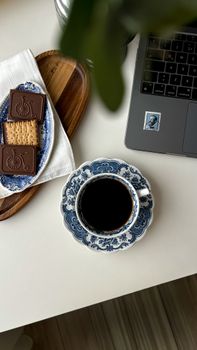 A stylish coffee scene with blue floral cup, biscuits, and a laptop for a cozy working atmosphere.
