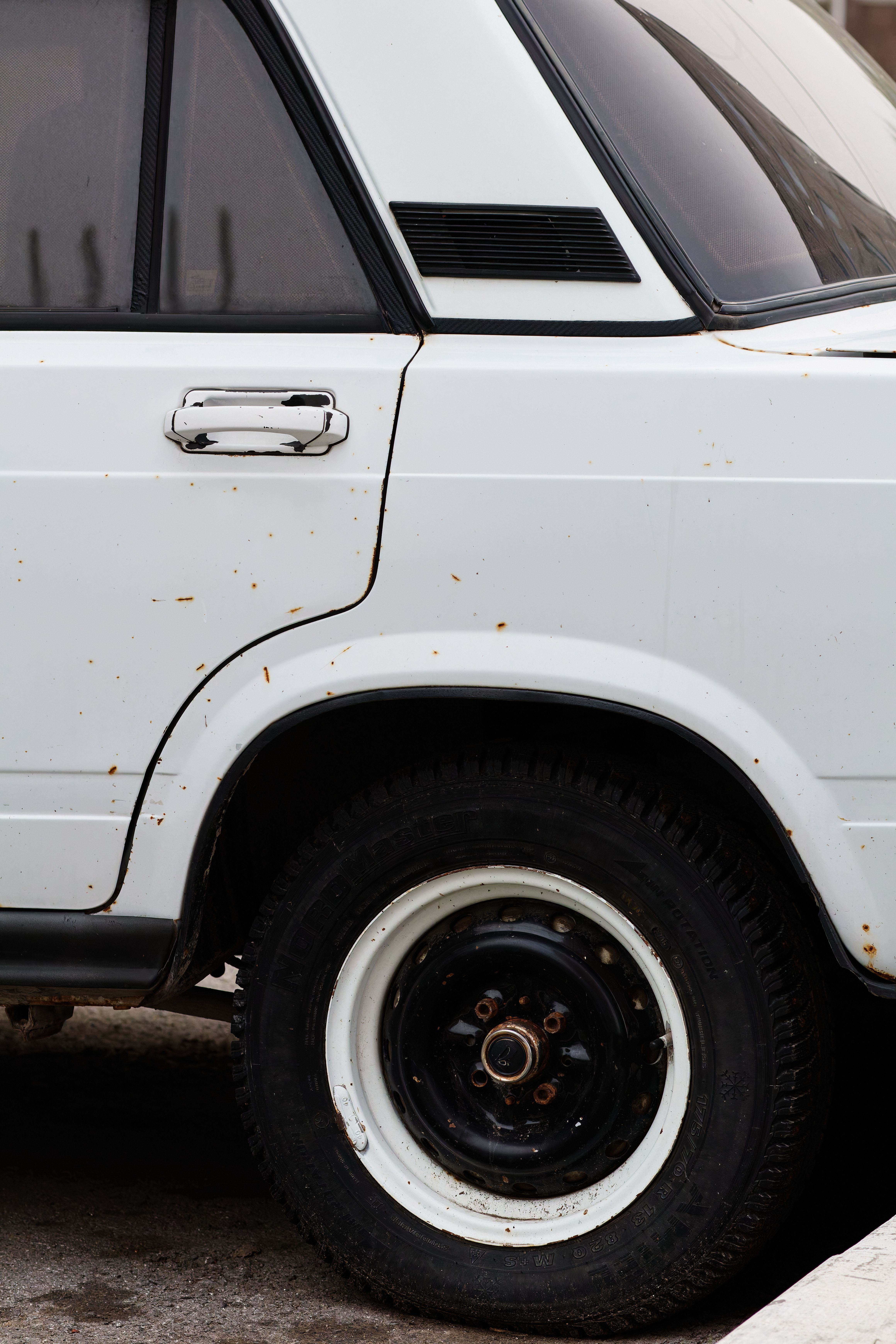 Close-up of a vintage white car showing rust spots on the wheel arch and side panel, illustrating the kind of corrosion buyers need to look for when inspecting a used vehicle