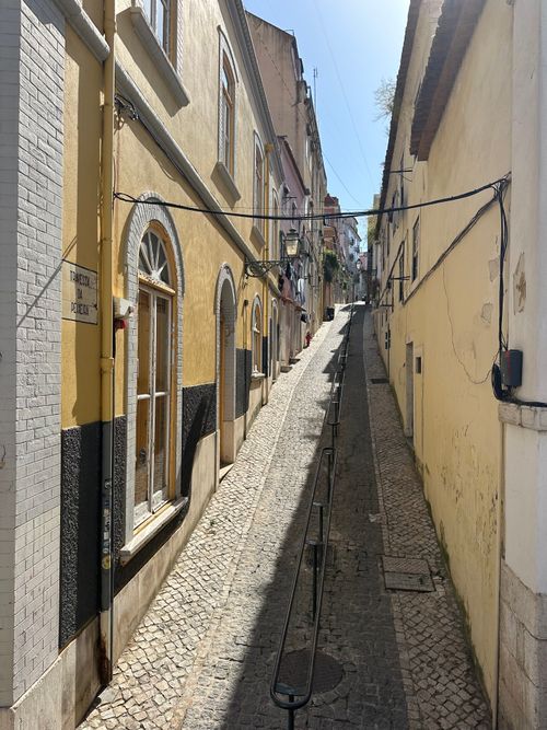Free Sunlit alleyway in Lisbon featuring traditional architecture and cobblestone path, creating a picturesque urban scene. Stock Photo
