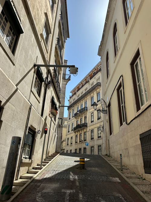 Free Sunlit alley in Lisbon showcasing historic European architecture and a clear blue sky. Stock Photo