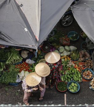 Top-down view of women in conical hats browsing a colorful vegetable market.