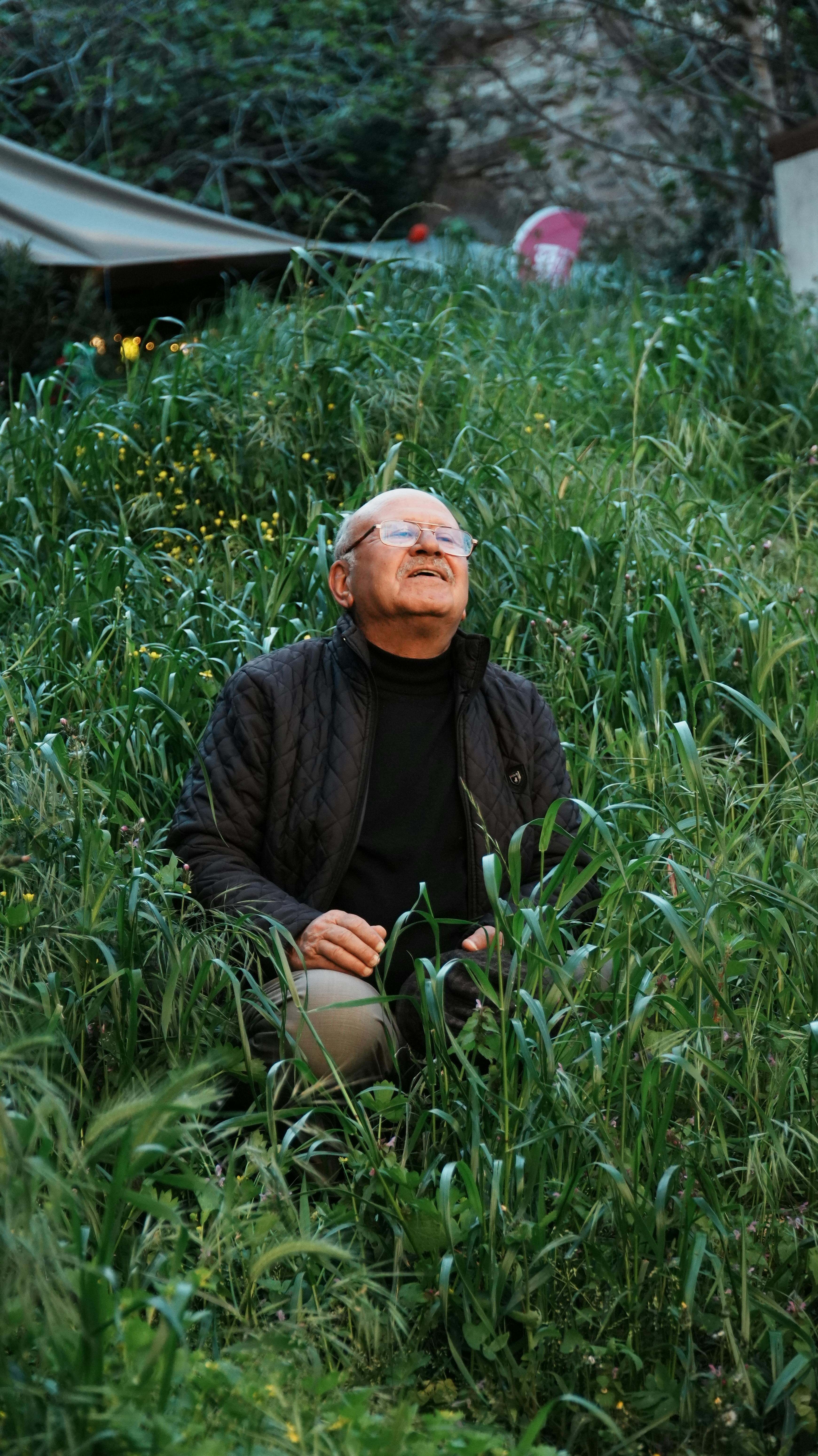 Elderly man seated in lush grass, reflecting amidst Istanbul's serene outdoor beauty.