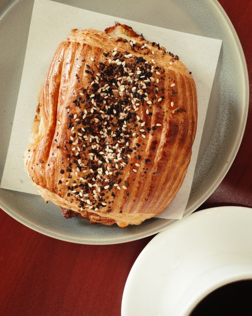 Free A close-up of a freshly baked seeded croissant on a plate with a cup of black coffee. Stock Photo