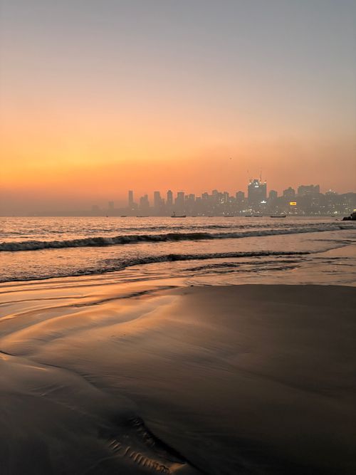 Free Beautiful sunset over Mumbai skyline from the beach, with calm waves reflecting orange hues. Stock Photo