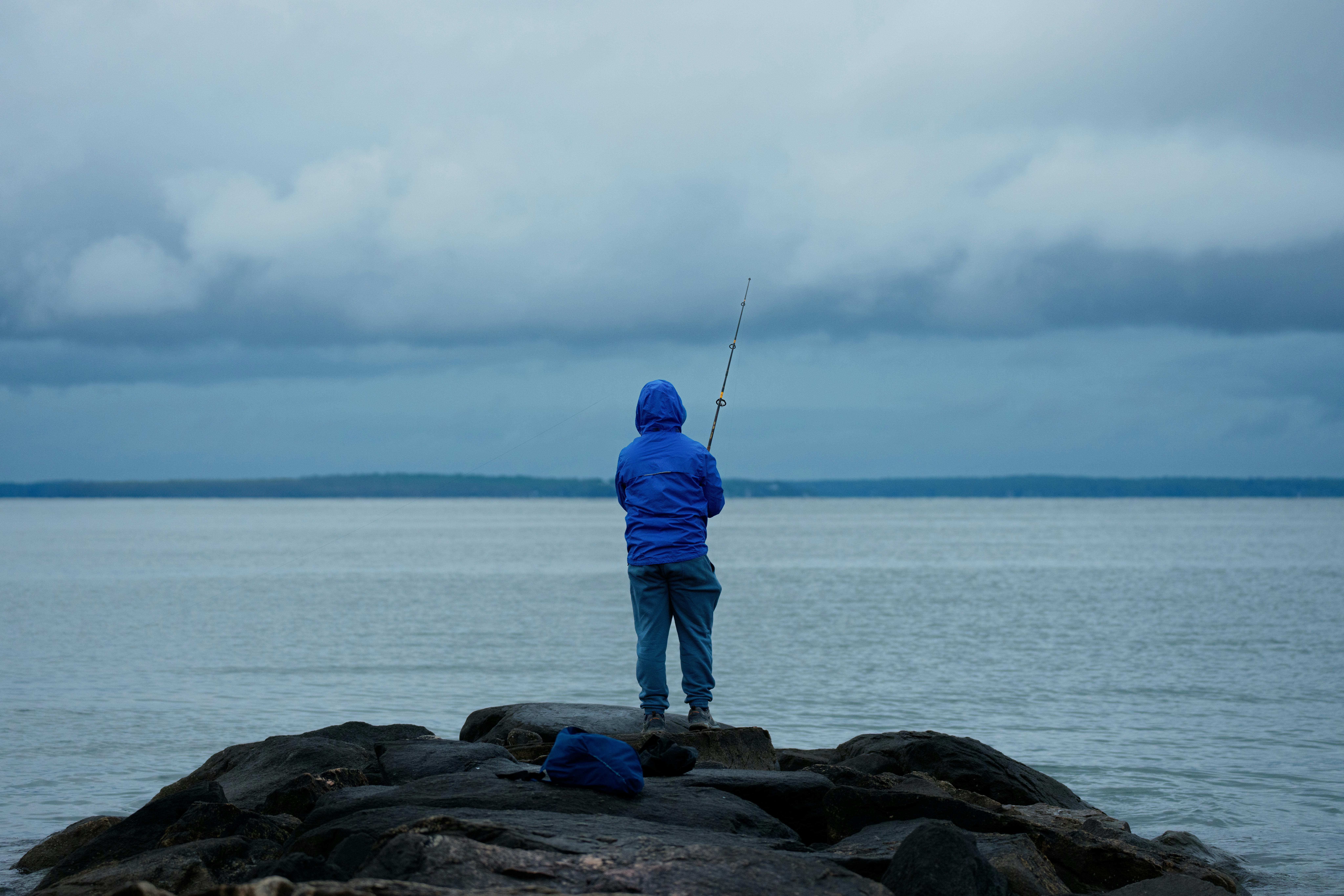 Angler wearing a life jacket and non-slip water shoes standing on wet jetty rocks near the ocean