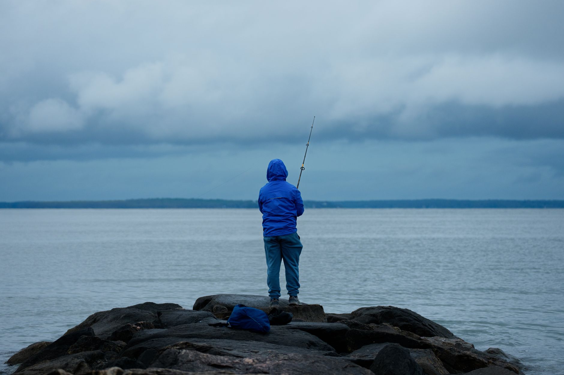 Angler wearing a life jacket and non-slip water shoes standing on wet jetty rocks near the ocean
