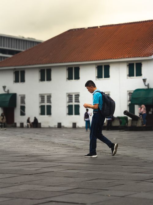 Free A young man walks in a historical courtyard in Jakarta, Indonesia, with a backpack. Stock Photo