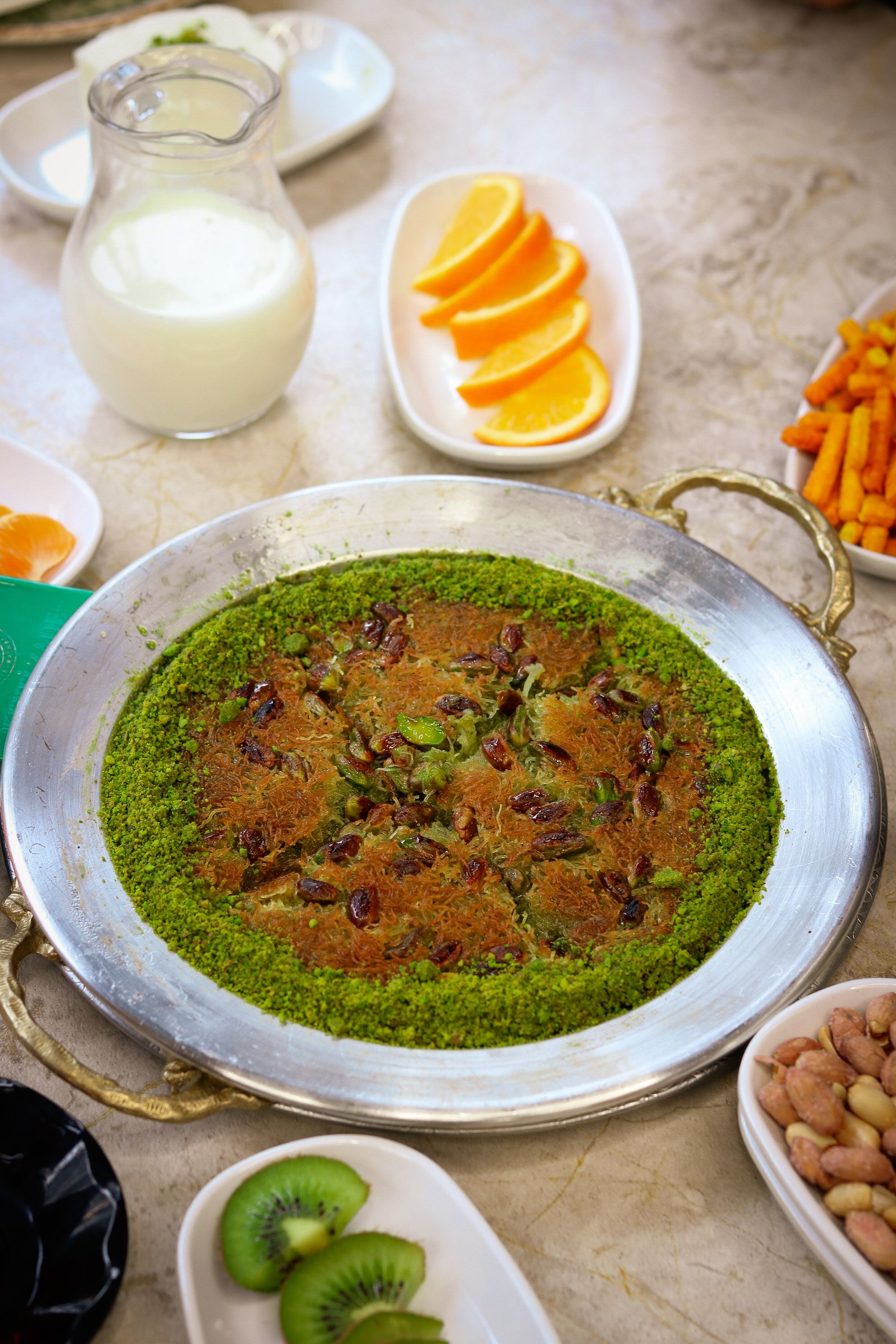 A vibrant pistachio dessert surrounded by fresh fruits and milk, perfect for a luxurious meal.