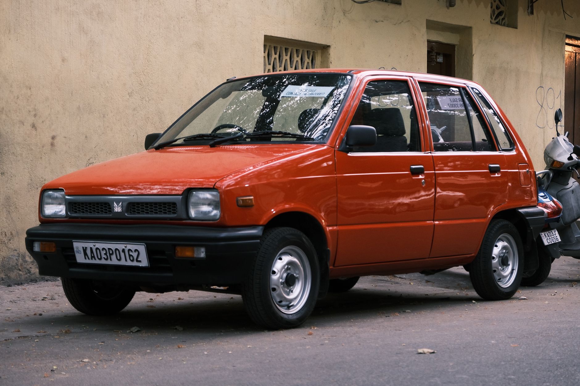 Classic red Maruti 800 parked on a Bengaluru street, showcasing vintage automotive style.