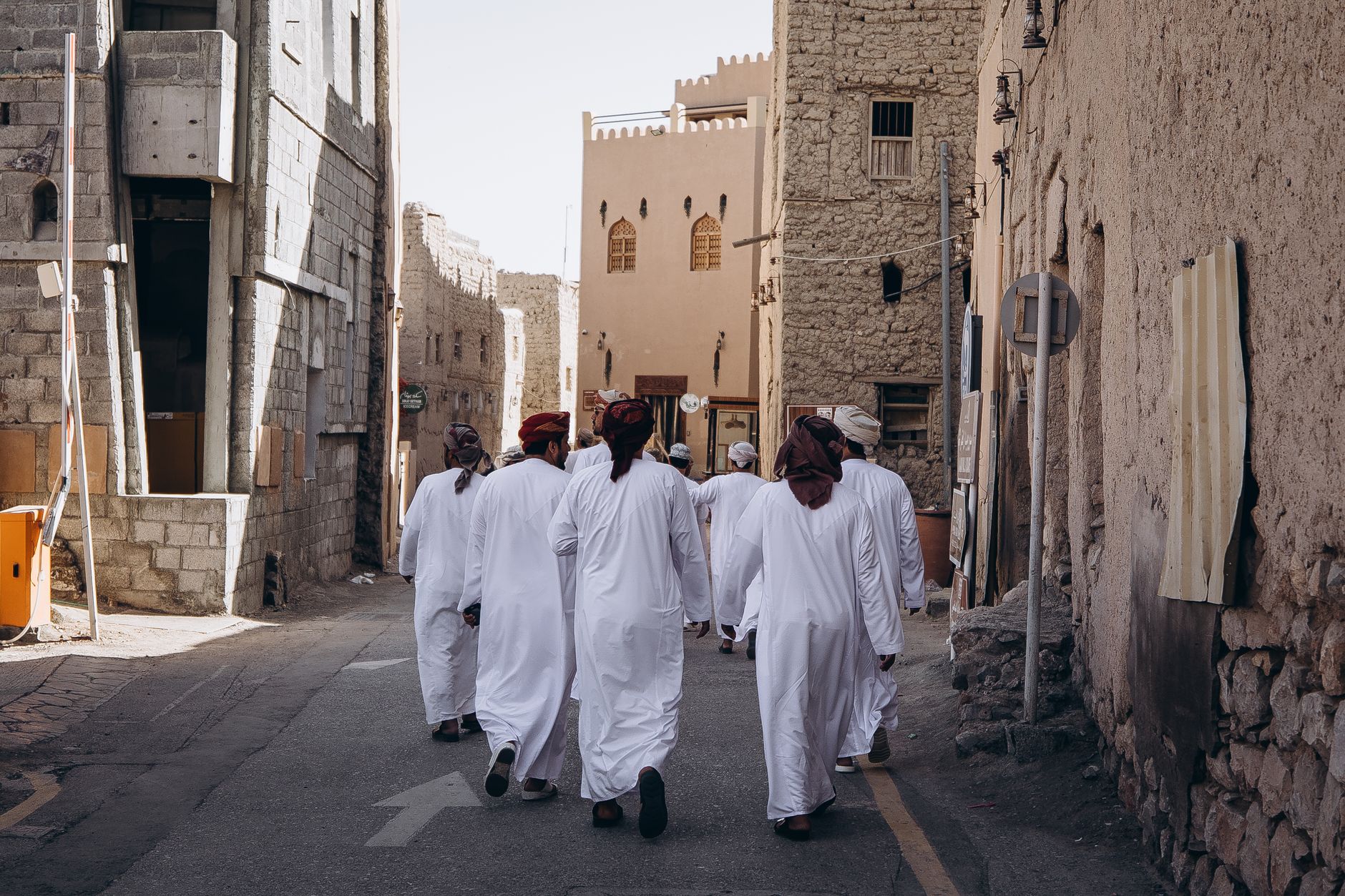 Men in traditional Omani attire walk through the historic streets of Nizwa, Oman, showcasing cultural heritage.
