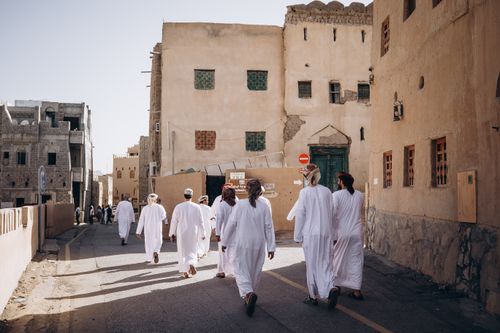 Free Adults in traditional attire walk through the old town of Nizwa, Oman, showcasing its rich cultural heritage. Stock Photo