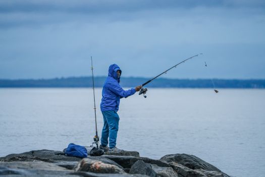 A person in blue fishing by the rocky shoreline with a tranquil lake in the background.